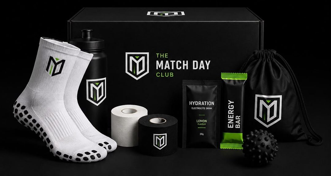 The Match Day Club box with grip socks, water bottle, sports tape, lemon hydration sachet, energy bar, recovery massage ball and a branded drawstring bag, all arranged on a black background.